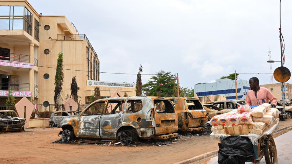 A street vendor pushes his cart past burnt cars outside the headquarters of ousted President Mohamed Bazoum's Nigerien Party for Democracy and Socialism in Niamey on August 7, 2023.